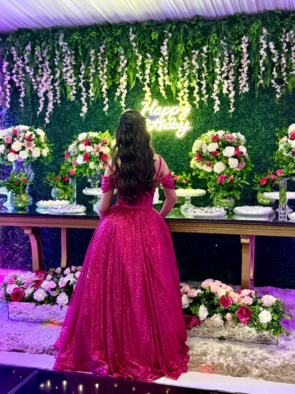 Debutante na mesa do bolo com parede de folhagem